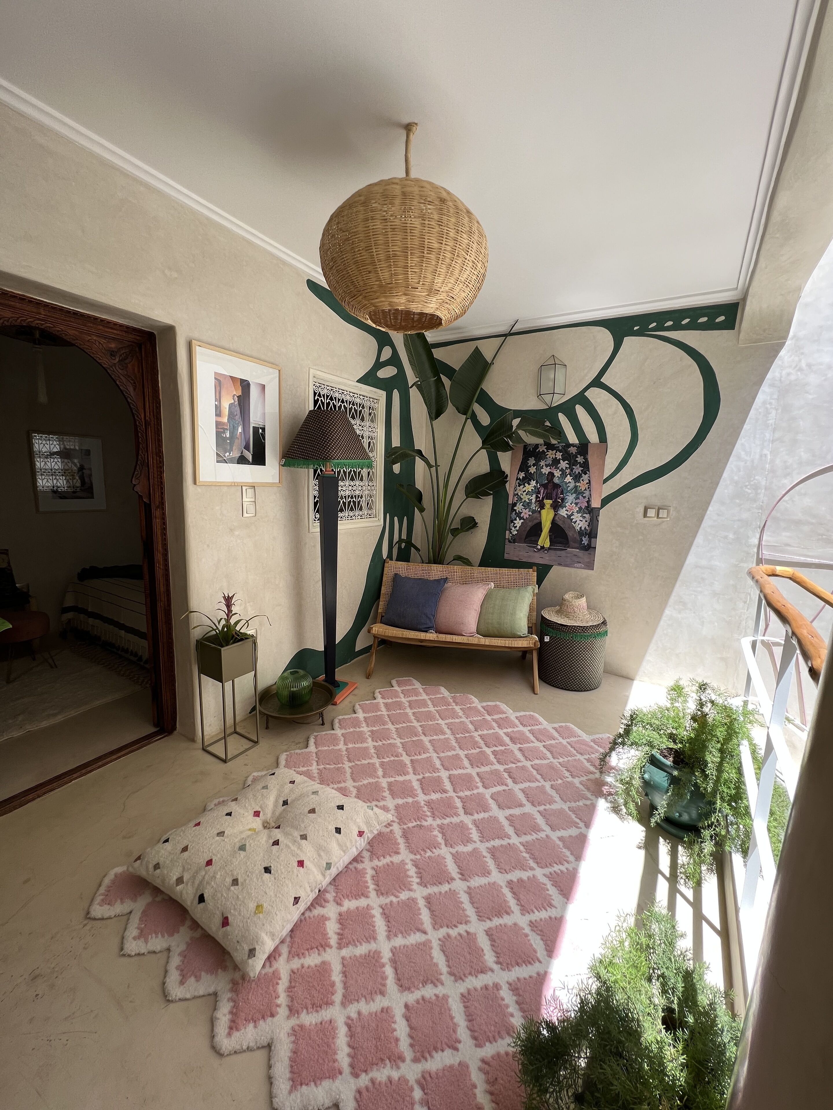 Une pièce chaleureuse avec un luminaire suspendu en fibres tressées, un canapé agrémenté de coussins, un tapis à motifs et une plante en pot.