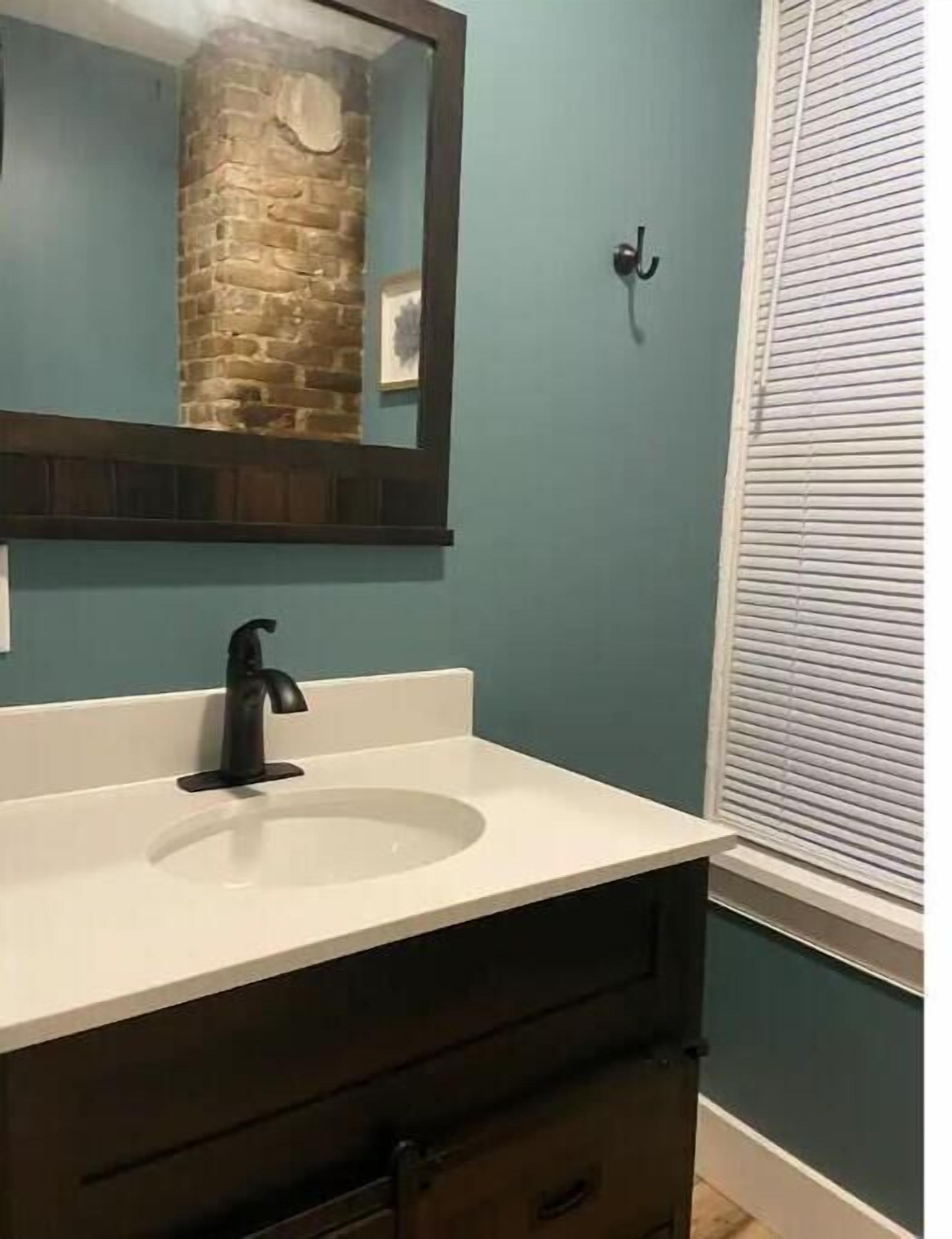 A bathroom with a white sink, dark cabinetry, a mirror, and a window with blinds.