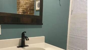 A bathroom with a white sink, dark cabinetry, a mirror, and a window with blinds.
