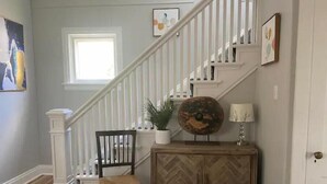 Un escalier avec des rampes blanches, une chaise en bois, une plante en pot, une assiette décorative et une lampe posée sur un meuble en bois.