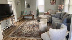 Un salon comprenant une télévision, un banc, un canapé, un tapis à motifs et un ventilateur de plafond.