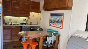 A compact kitchen with wooden cabinets, a tiled backsplash, and a dining area with a table and orange stools.