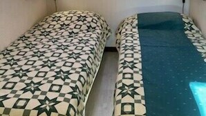 A small room with two beds, each with patterned bedding, a skylight, and two wall-mounted lamps.