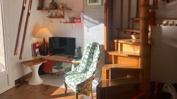 A cozy living room with a television, a chair, and skis leaning against the wall.