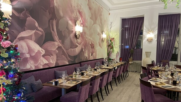Un comedor con mesas largas, sillas tapizadas de color morado y un gran mural floral en la pared.