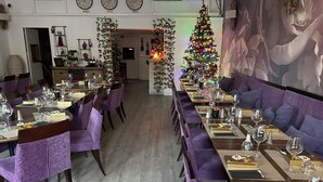 Un restaurante con mesas largas, sillas tapizadas en morado y un árbol de Navidad con luces.
