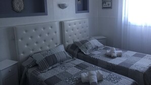 Un dormitorio con dos camas, cabeceros, mesitas de noche y una ventana con cortinas.