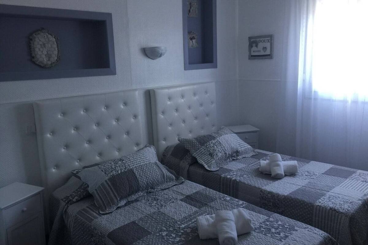 A bedroom with two beds, a headboard, a nightstand, and a window with curtains.