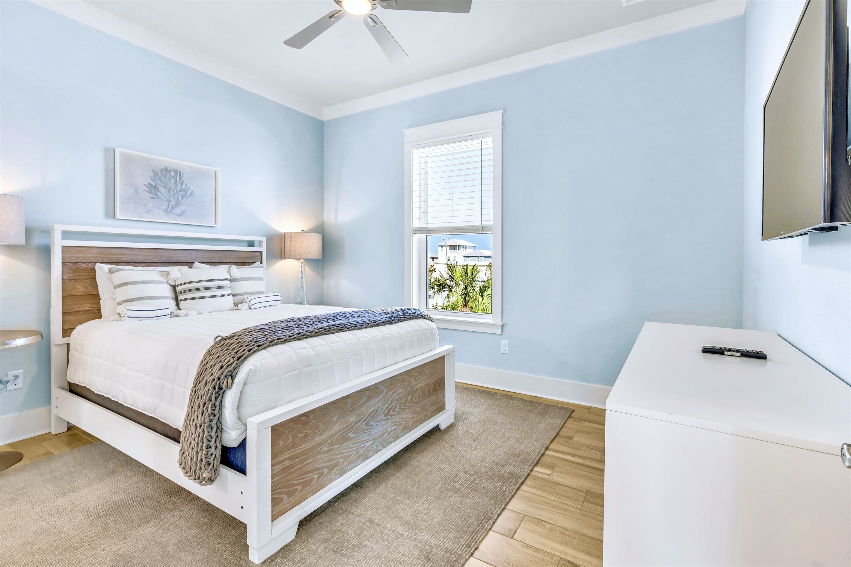 A bedroom with a bed, bedside lamps, a ceiling fan, a window, and a TV on a stand.