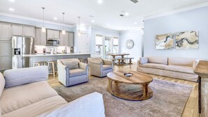 A spacious living room with a large sofa, a coffee table, and a dining area with a table and chairs. - Sea Glass: Free golf cart, 2min to beach, Heated pool steps away, Bunk rooms (Miramar Beach)