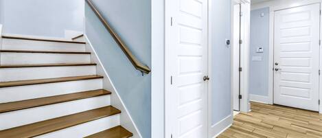Un escalier avec des marches en bois et une rampe métallique, menant à un couloir avec des portes blanches et un mur bleu clair.