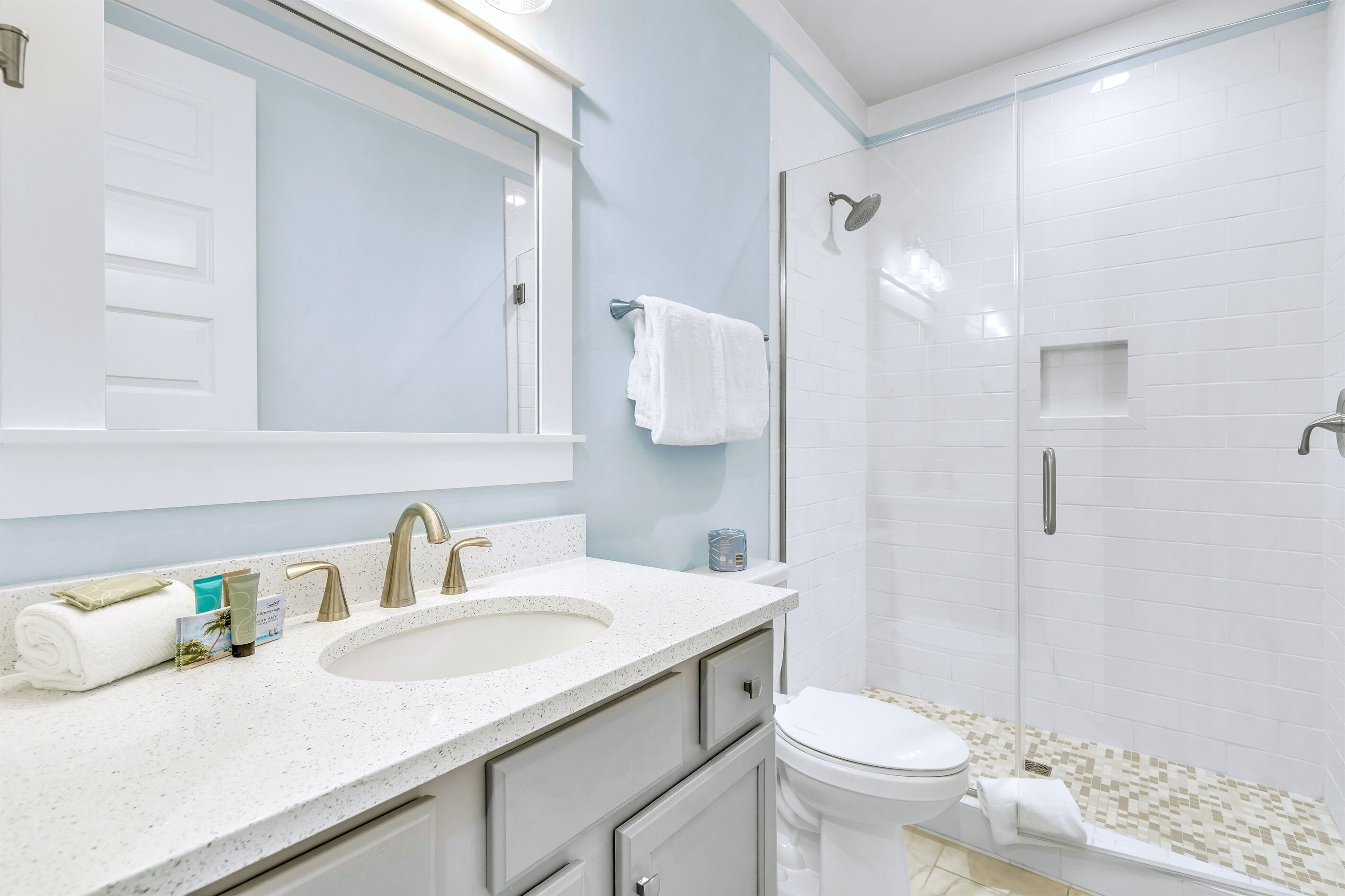 Une salle de bain moderne avec un lavabo blanc, deux robinets, un grand miroir et une douche à parois de verre.