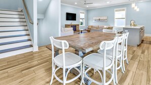 A spacious living room with a wooden dining table, white chairs, a sofa, and a kitchen area with a sink and counter. - Sea Glass: Free golf cart, 2min to beach, Heated pool steps away, Bunk rooms (Miramar Beach)