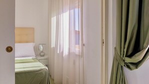 Une chambre d’hôtel avec un lit, une table de chevet, une lampe et des rideaux en voile.