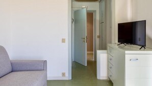 Une pièce avec un canapé gris, un téléviseur posé sur un meuble et une porte donnant sur une autre pièce.