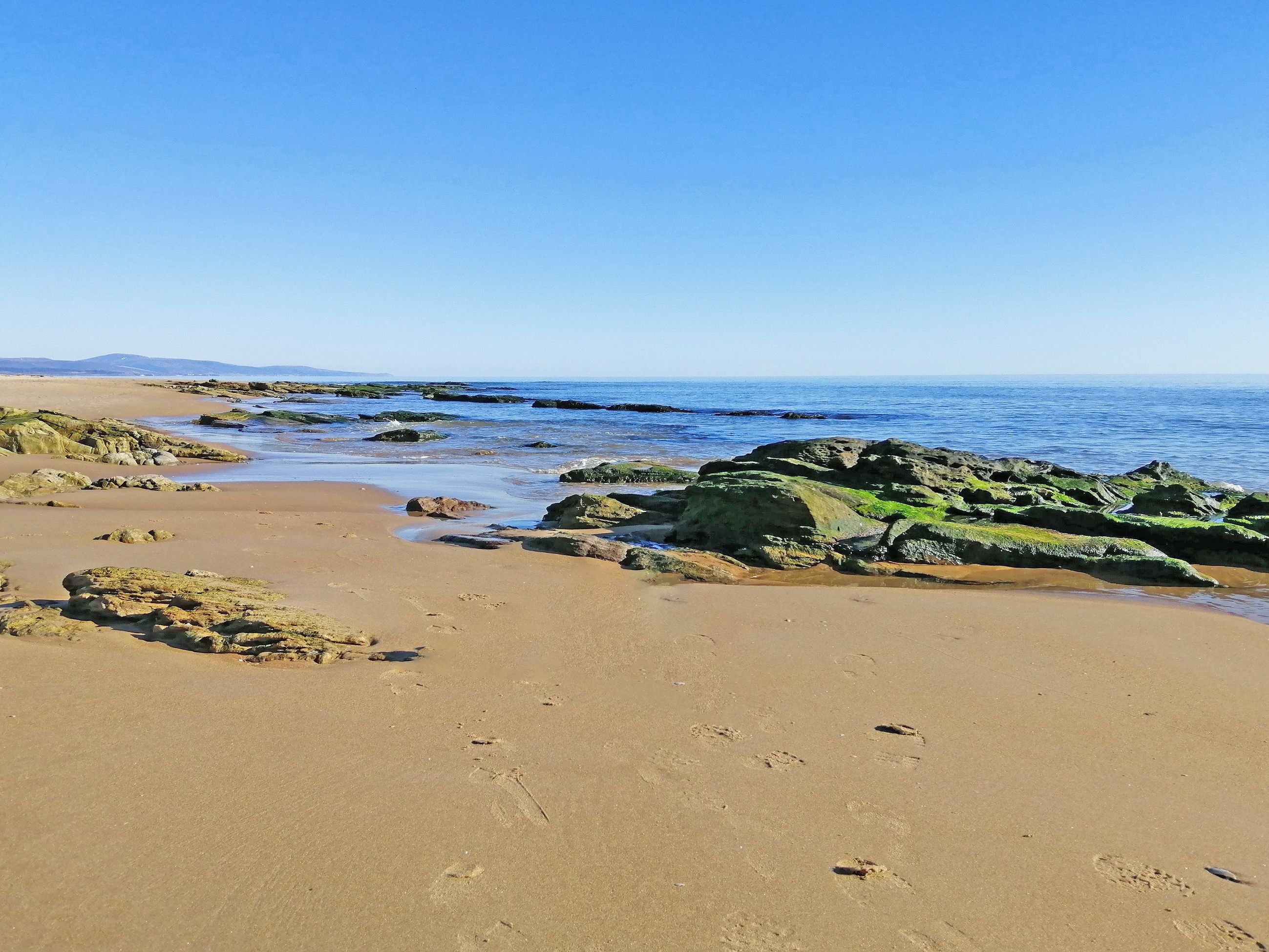 A beach with rocky outcrops and clear blue water.
