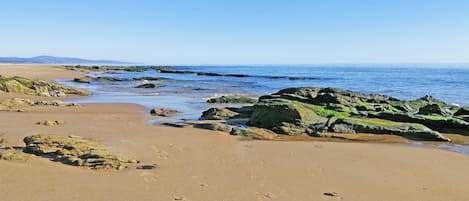 Een strand met rotsformaties en helderblauw water.