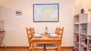 Un comedor con una mesa de madera preparada para dos personas, un mapa en la pared y una estantería con libros y adornos.