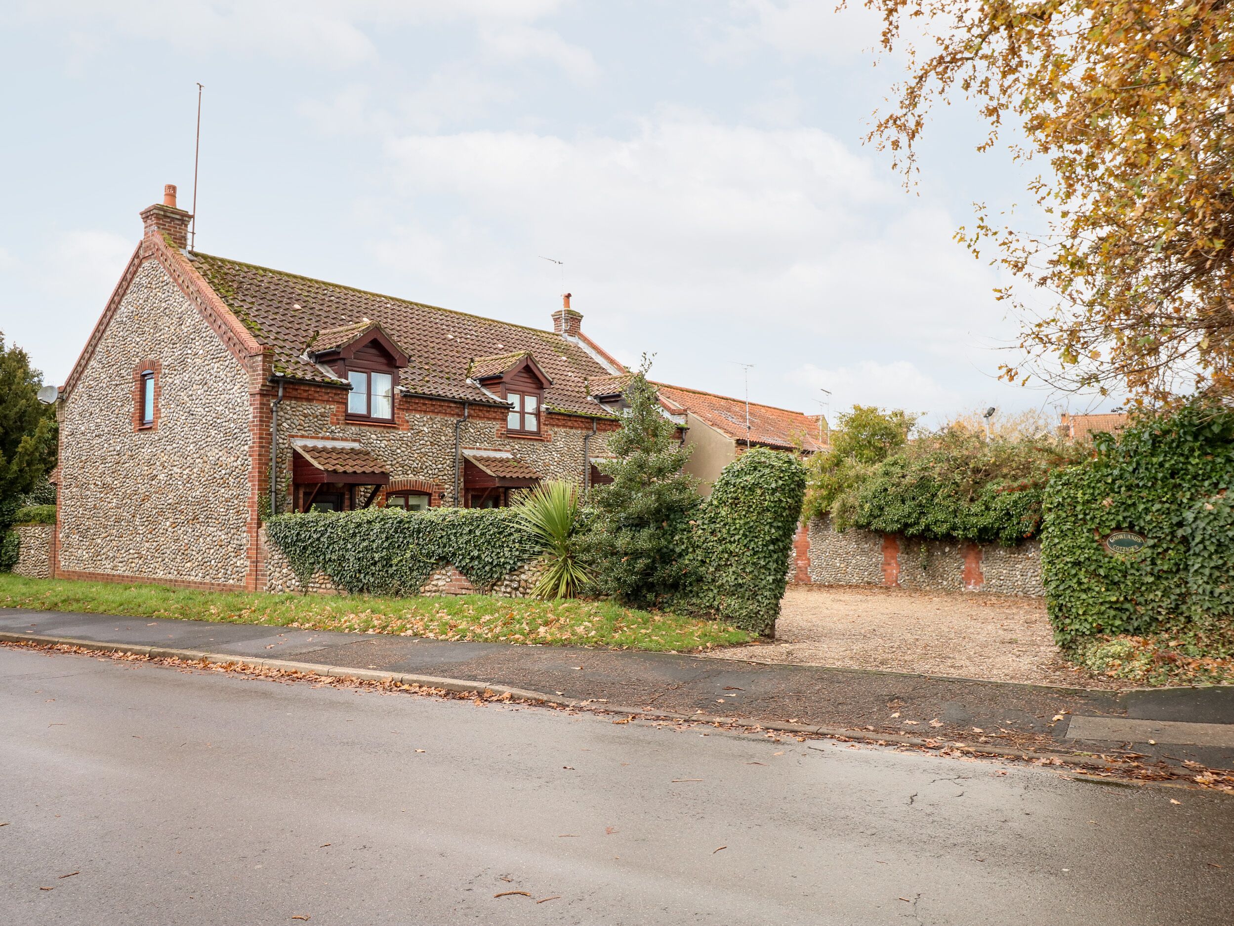 A stone house with a tiled roof, a chimney, and a small garden with a hedge and a tree.