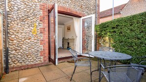A patio with a stone wall, a brick fireplace, and a table with chairs. - 1 Crowlands Cottages (Holt)