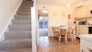 A staircase leading to a dining area with a table and chairs, a kitchen with cabinets and appliances, and a view of the outside through a glass door. - 1 Crowlands Cottages (Holt)