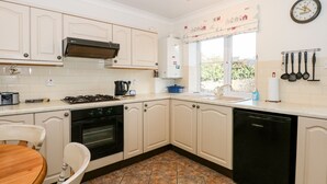 A kitchen with white cabinets, a stove, oven, dishwasher, and a window with a view. - 1 Crowlands Cottages (Holt)