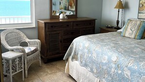Une chambre à coucher comprenant un lit, une commode, une chaise et une grande fenêtre donnant sur l’océan.