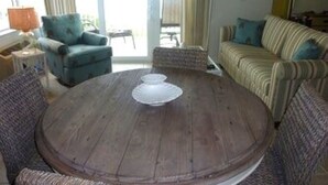 Une table ronde en bois, entourée de chaises, dans une pièce où se trouvent un canapé et des rideaux.