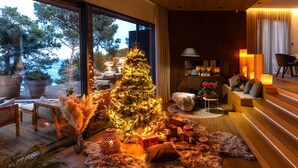A modern living room with a large Christmas tree, wooden flooring, and a view of the outdoors.