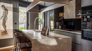 A modern kitchen with a large island, bar stools, a coffee machine, and a view of the outdoors.