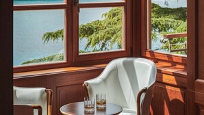 A room with a view of a body of water and greenery through large windows. There is a round table with two glasses on it. - Villa Mirasol - Eight Bedroom Villa, Sleeps 16 (Mali Losinj)