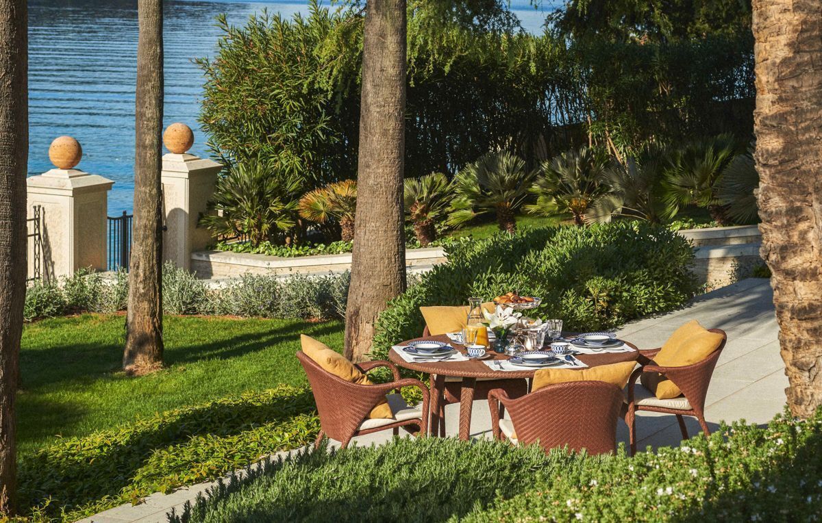 Un espace de restauration en plein air avec une table dressée pour deux personnes, entouré d’une végétation luxuriante et de palmiers.