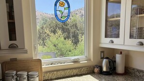 A kitchen with a window view of a forest, a countertop with jars, and a coffee maker. - Cozy secluded cabin on a working cattle ranch (Clifton)