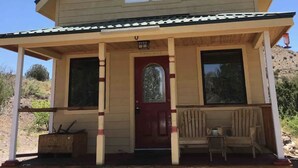 A two-story house with a front porch, a red door, and two windows on the upper floor. - Cozy secluded cabin on a working cattle ranch (Clifton)