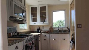 A kitchen with white cabinets, a stove, and a window. - Cozy secluded cabin on a working cattle ranch (Clifton)