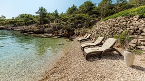 Une plage de galets avec des chaises longues et un mur de pierres.