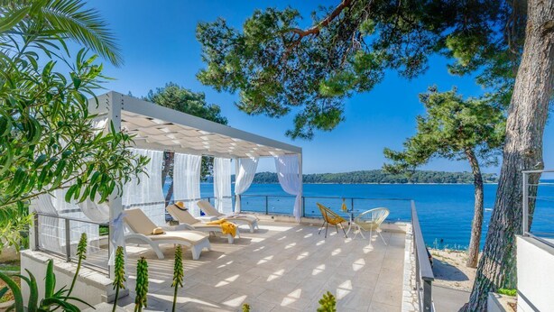 A terrace with sun loungers and a pergola overlooking a body of water.