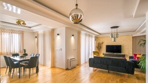 A spacious living area with a dining table, black sofas, and a flat-screen TV.