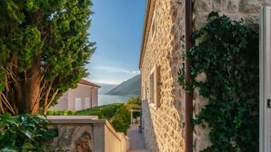A narrow stone pathway leading to a building with a stone facade and a view of the sea.