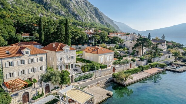 A coastal town with stone buildings, a marina, and a mountainous backdrop.