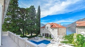 A stone villa with a swimming pool, surrounded by trees and a view of the sea.