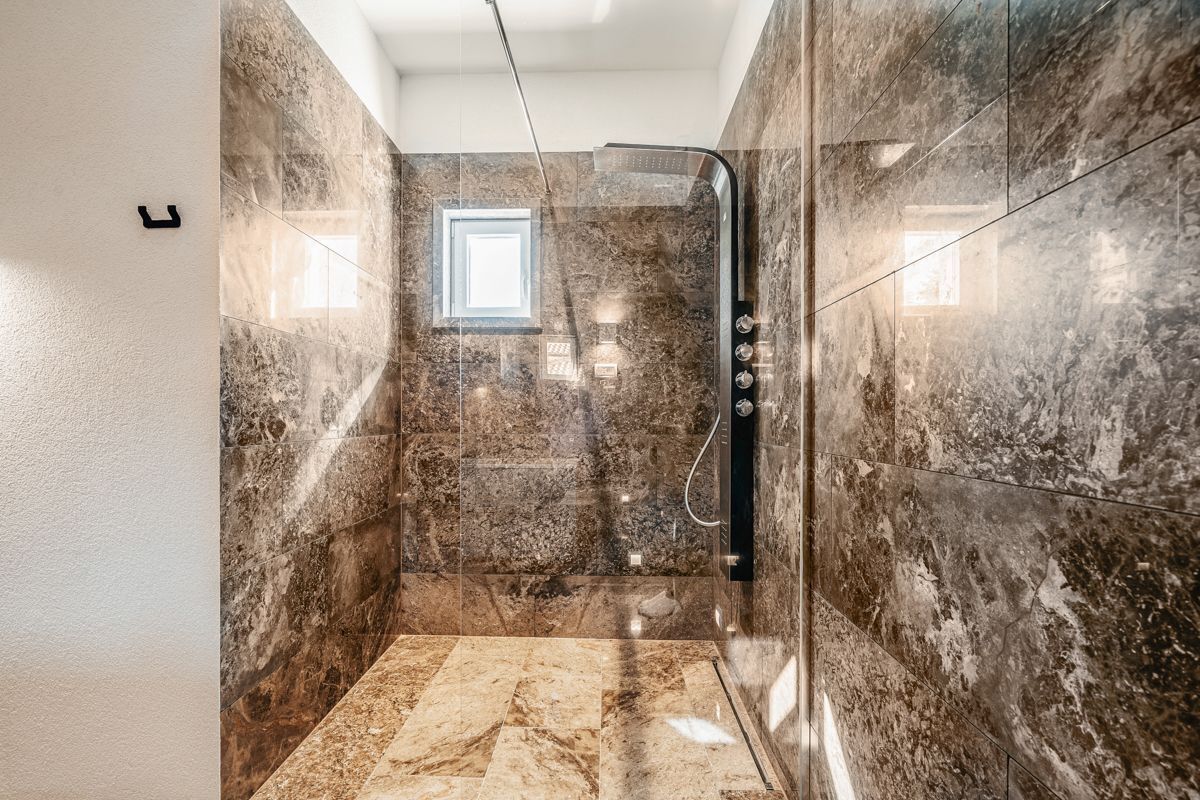 A modern bathroom with a shower area, marble walls, and a small window.