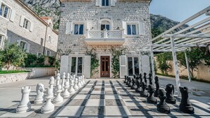 A stone building with a balcony, a chessboard with chess pieces, and a mountain in the background.