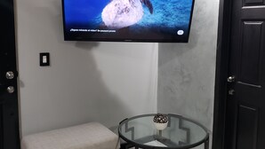 A living room with a flat-screen TV mounted on the wall, a glass coffee table, a beige sofa, and a dark wooden door. - Private Gorgeous Cozy Modern home/5 min Drive from beach, righ across from park (Tijuana)