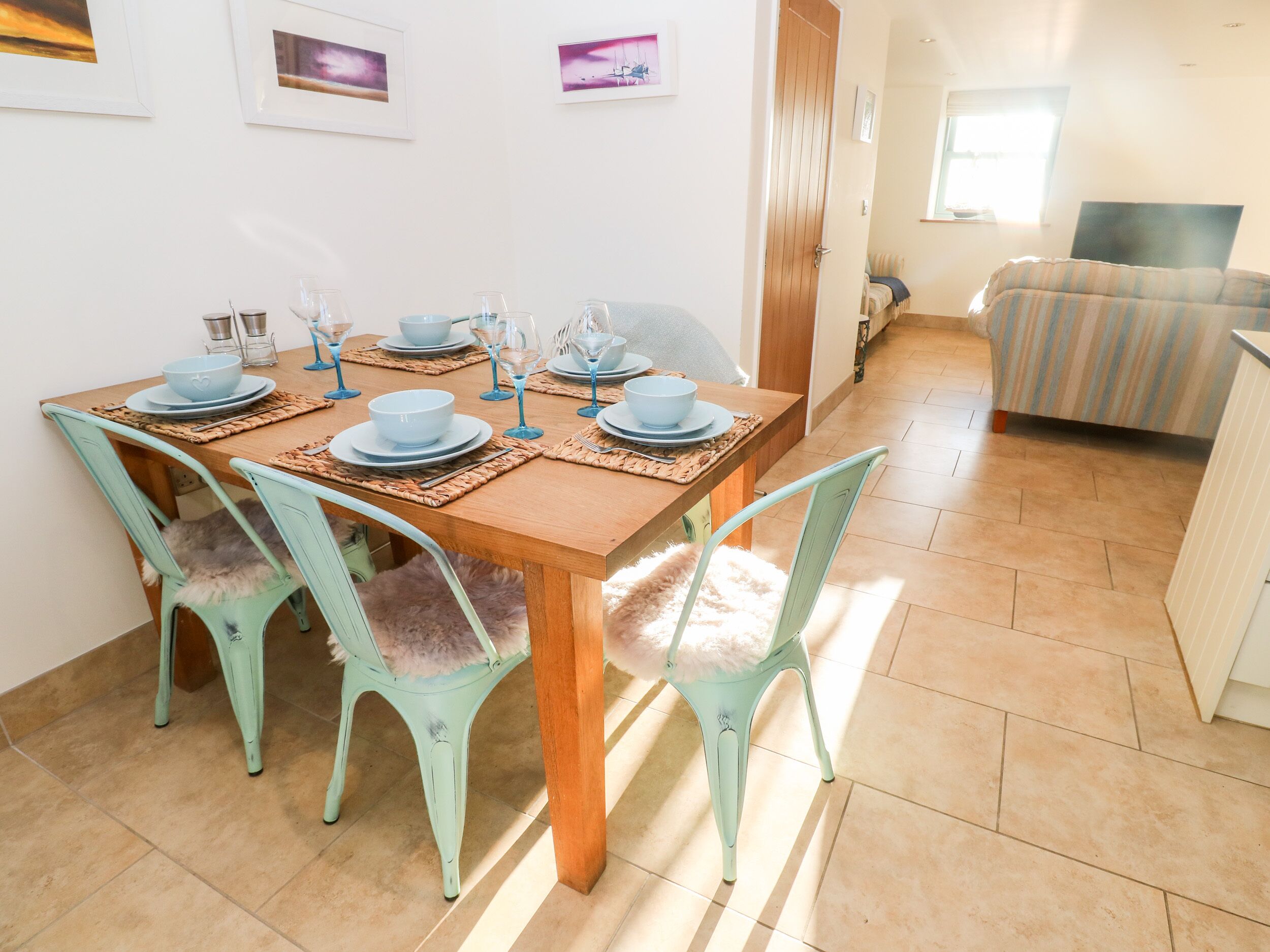 A dining area with a wooden table set for four, surrounded by four light green chairs with fluffy seats.