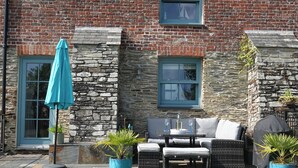 Een gebouw van steen met een bakstenen gevel, een terras met rieten meubels en een blauwe parasol.