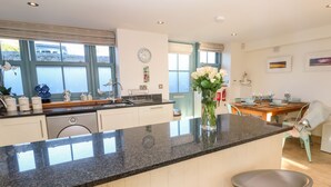 Een moderne keuken met een granieten aanrecht, witte kastjes en een eethoek met een houten tafel en barstoelen.