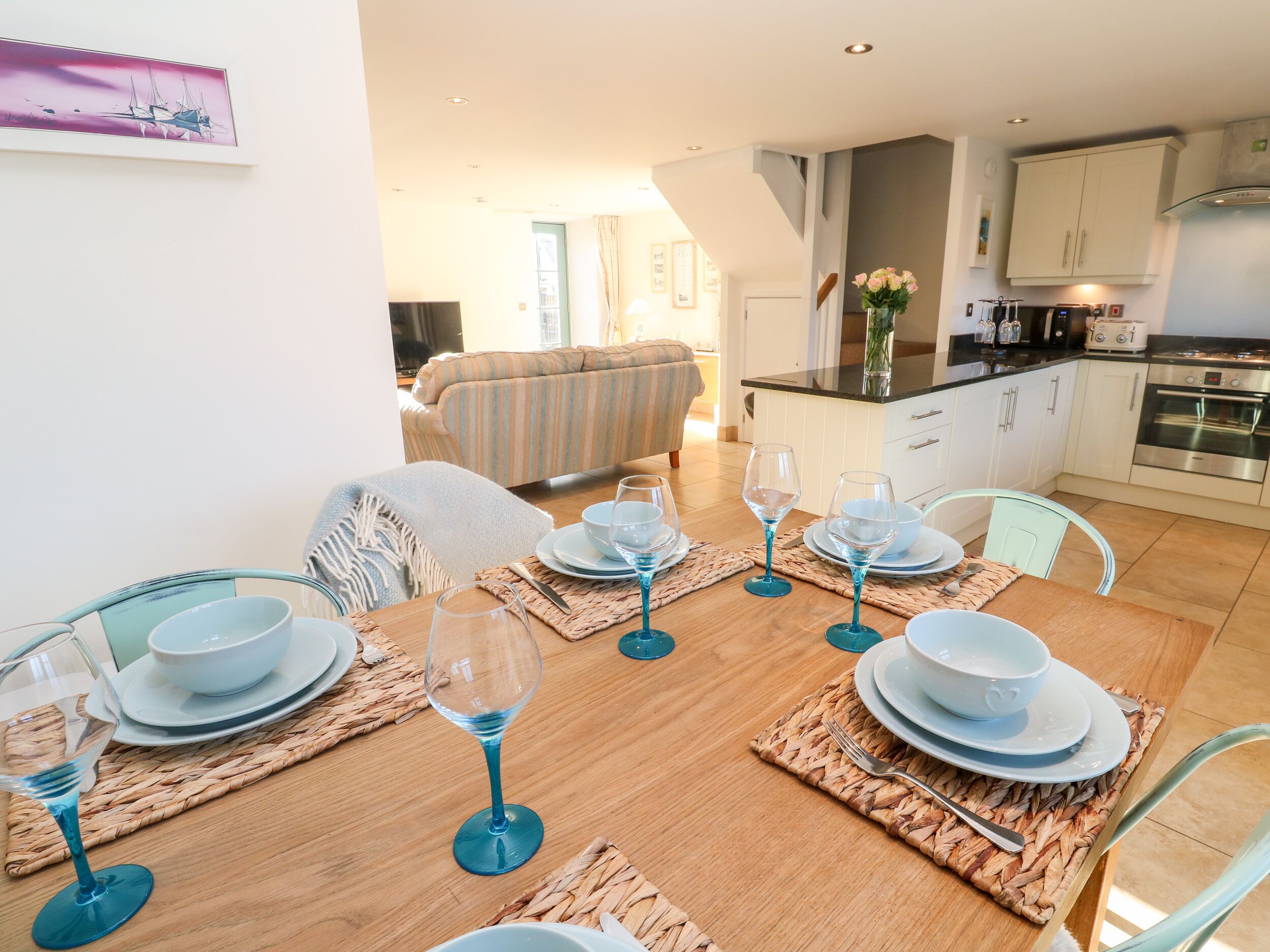 A dining area with a wooden table set for four, surrounded by chairs.