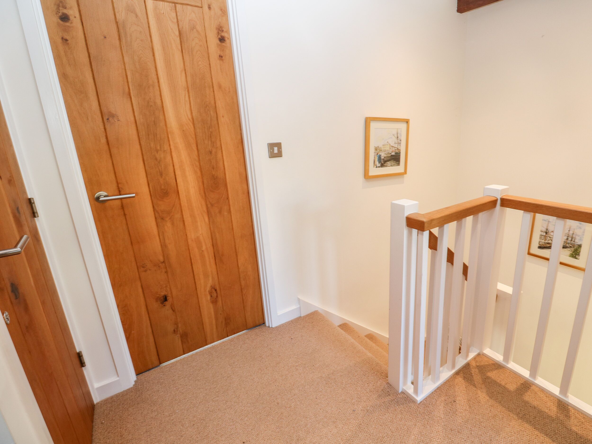 A wooden door with a white frame, a white wall with a picture, and a white railing with a wooden handrail.
