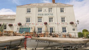 Een wit gebouw met de tekst 'Pier House' en 'Stustell Brewery' op de gevel. Voorin staan twee boten, genaamd 'Spirit' en 'Rashleigh', op een aanhanger.